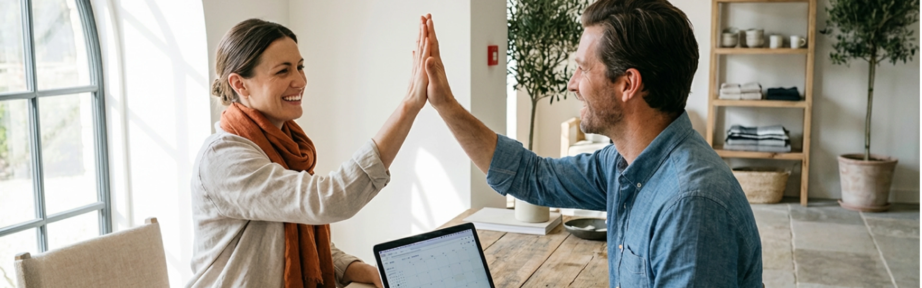 Two hoteliers high-fiving while looking at a laptop