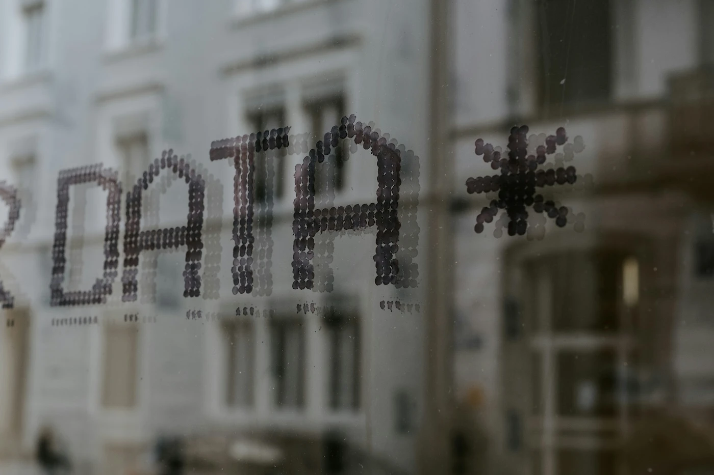 Close-up of 'DATA*' formed by small dots on a glass window, with blurred reflections of city buildings in the background.