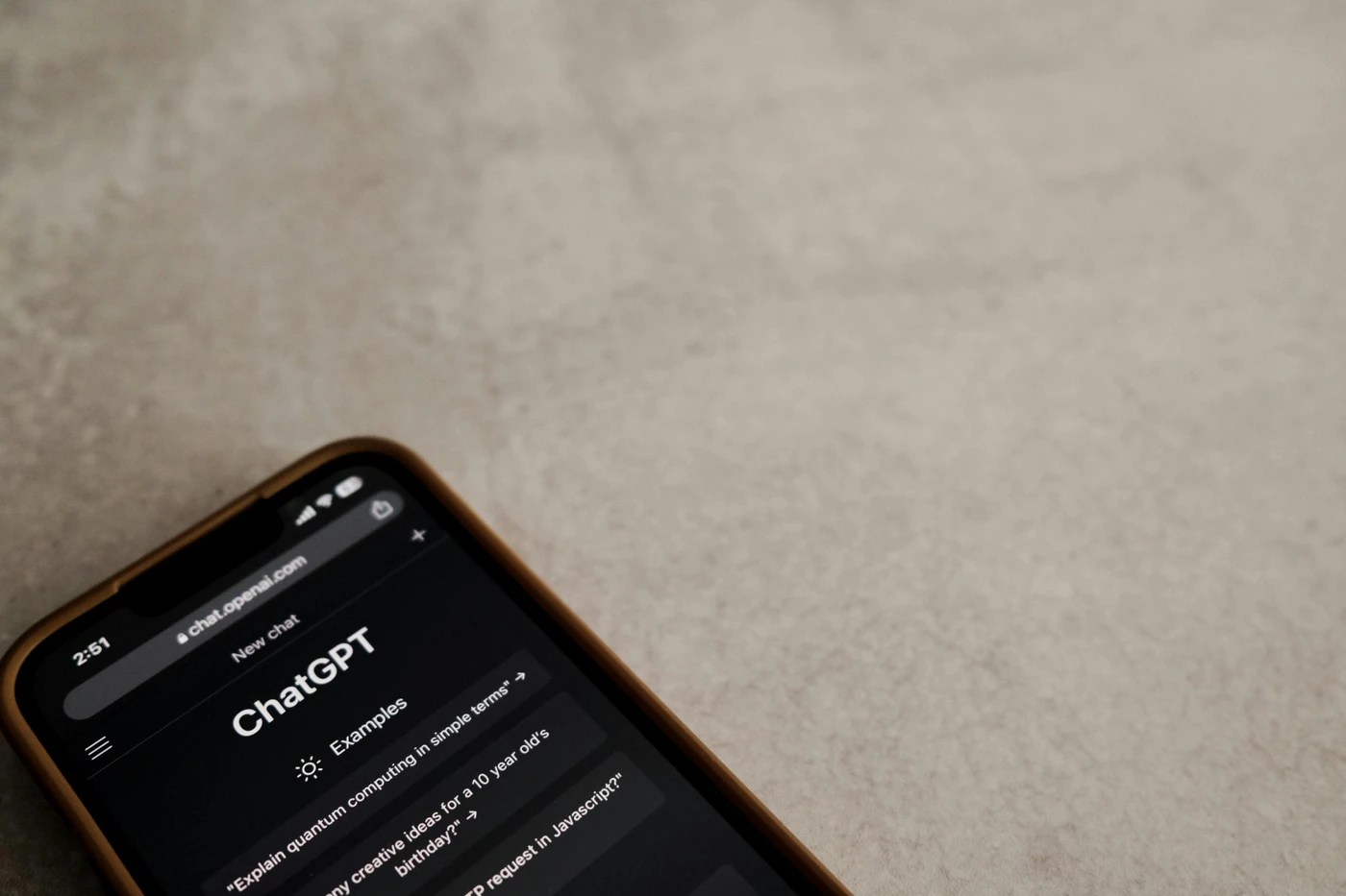 Smartphone on a beige textured surface displaying the ChatGPT web interface in dark mode.