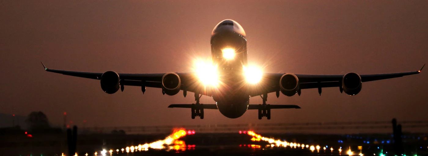 Passenger jet with bright landing lights approaches the runway at dusk, runway lights glowing beneath.