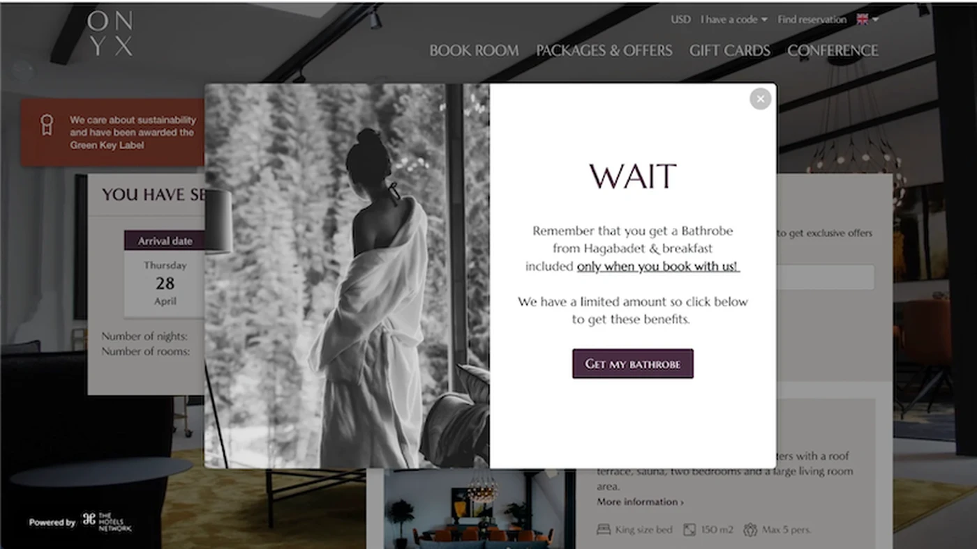 Pop-up message overlay on a hotel booking website, highlighting a bathrobe offer. Background shows a woman in a robe and room details.