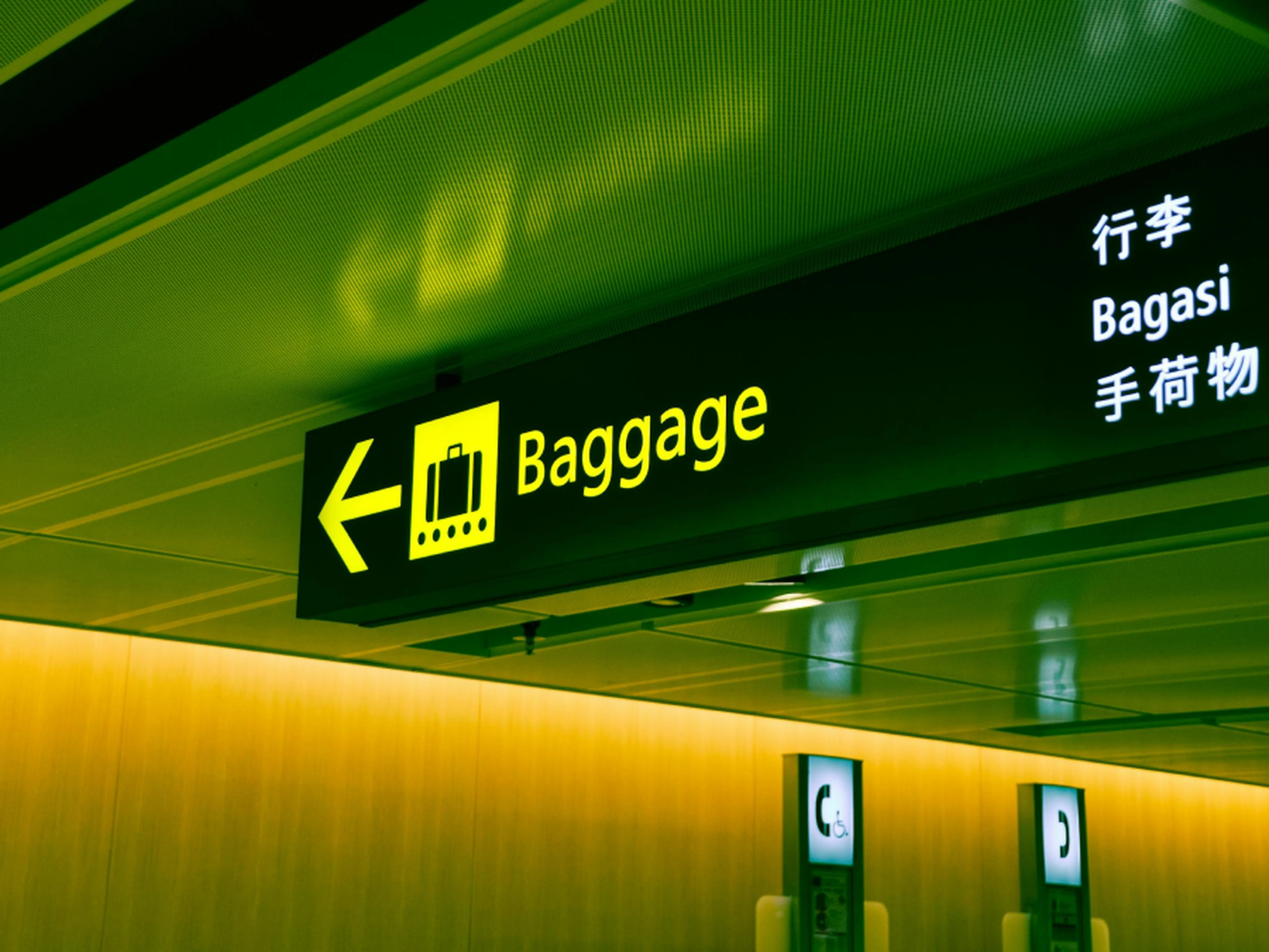 Yellow airport sign with a suitcase icon indicating baggage claim, featuring directions in English, Chinese, and Japanese.
