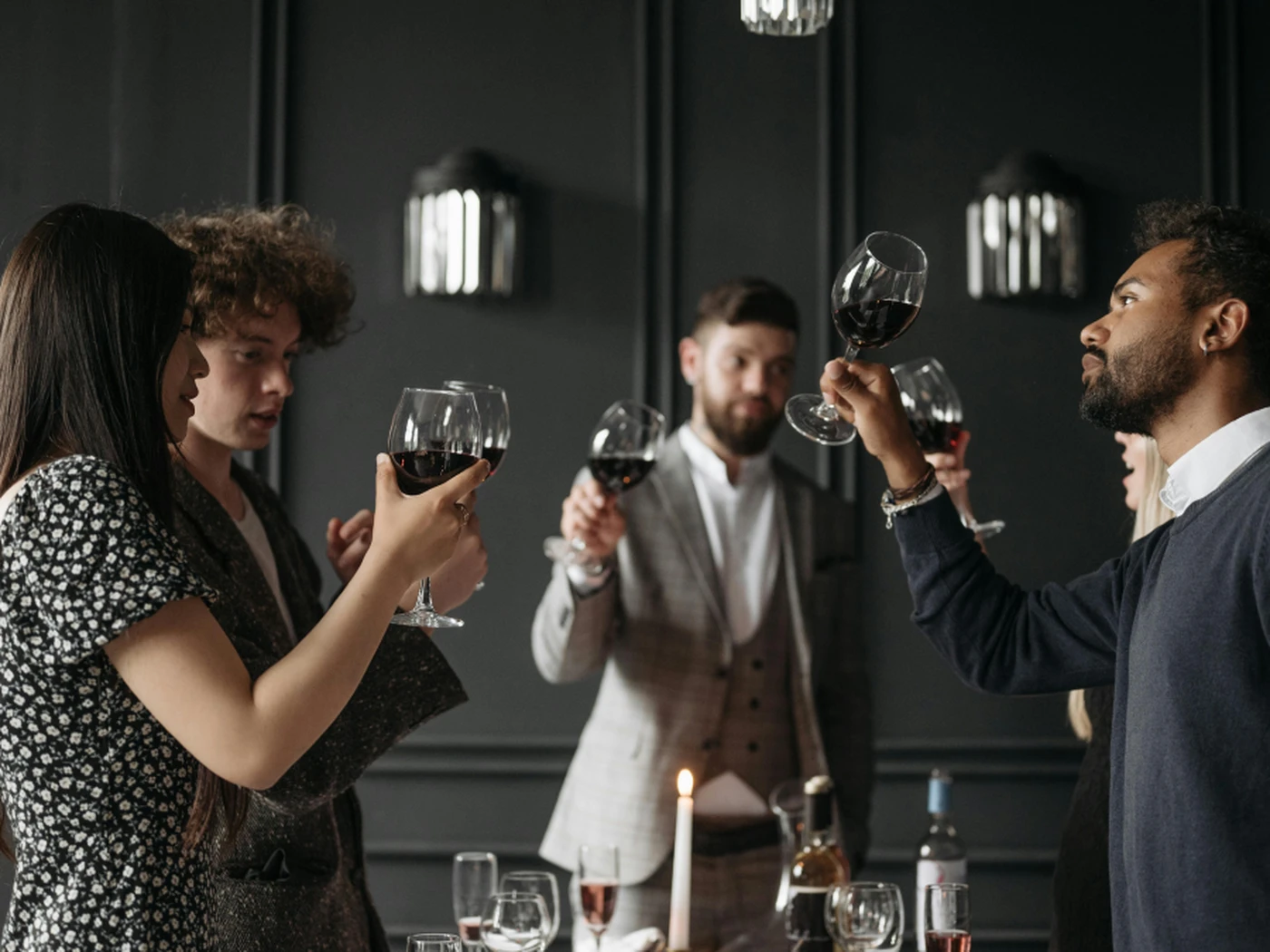 Hotel guests at a wine tasting around a candlelit table, set against a dark, elegant background.