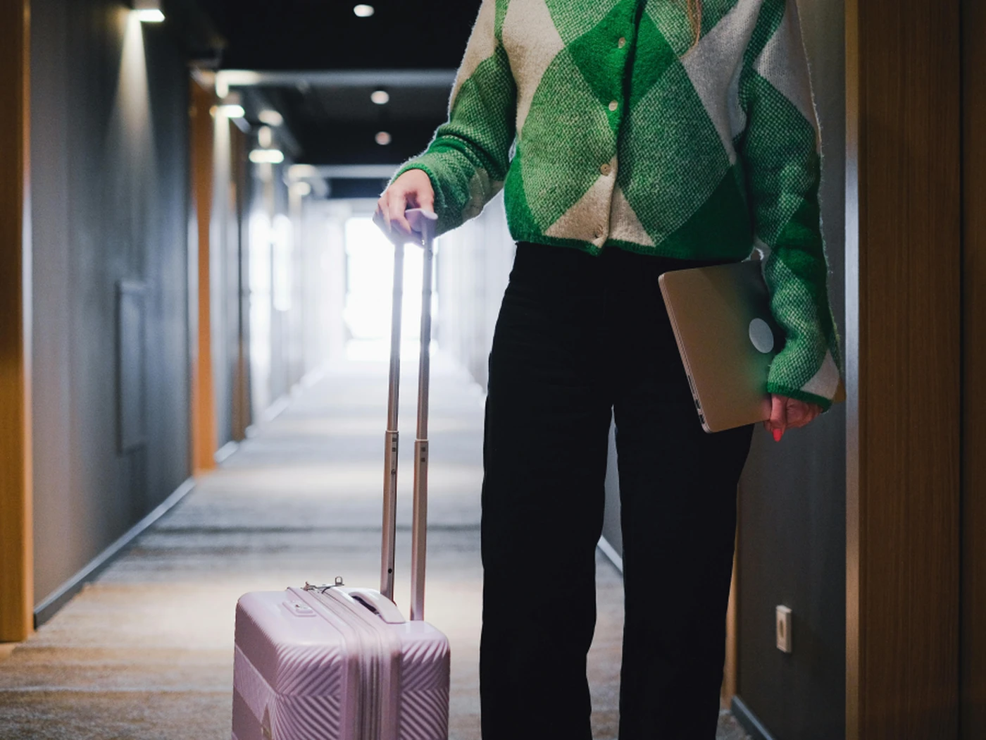 A guest holding her laptop and suitcase walks through the corridor of a hotel
