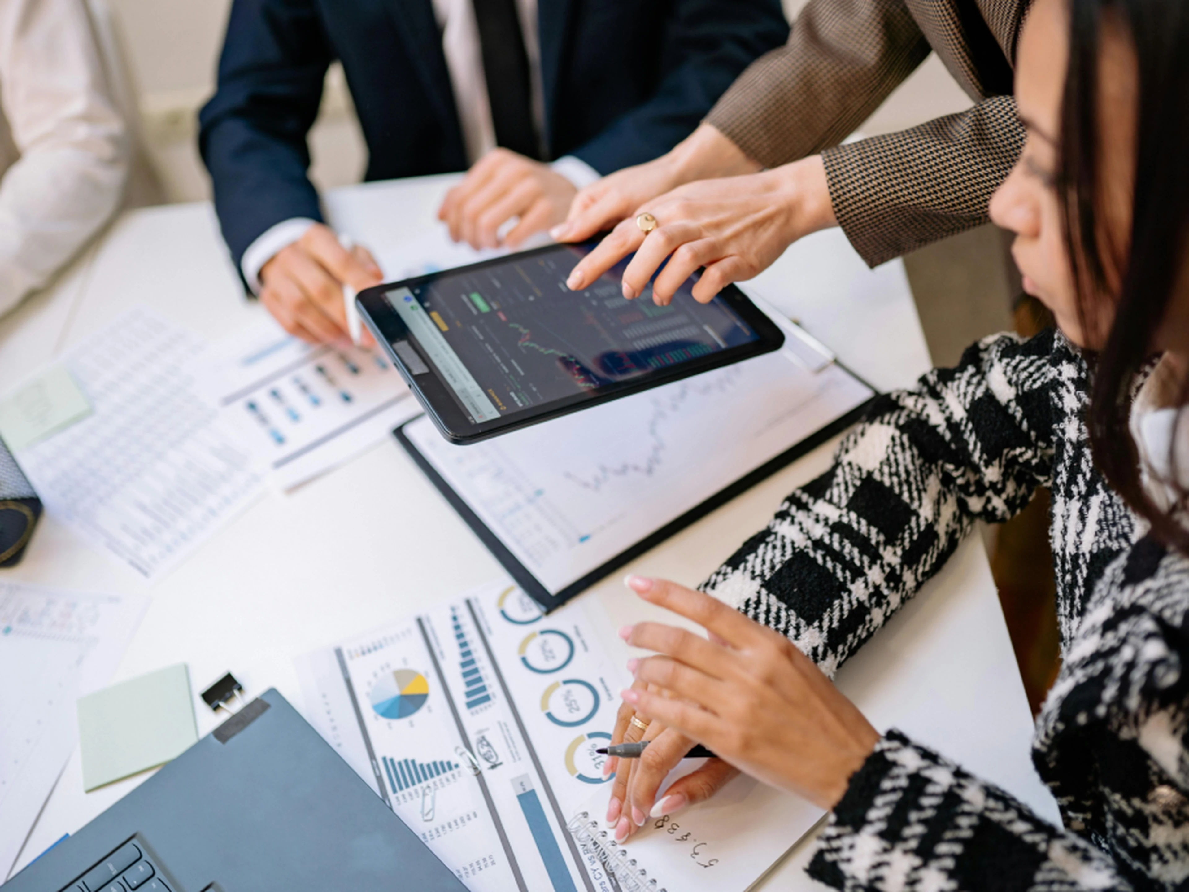 People in business attire review charts and graphs on paper and a tablet