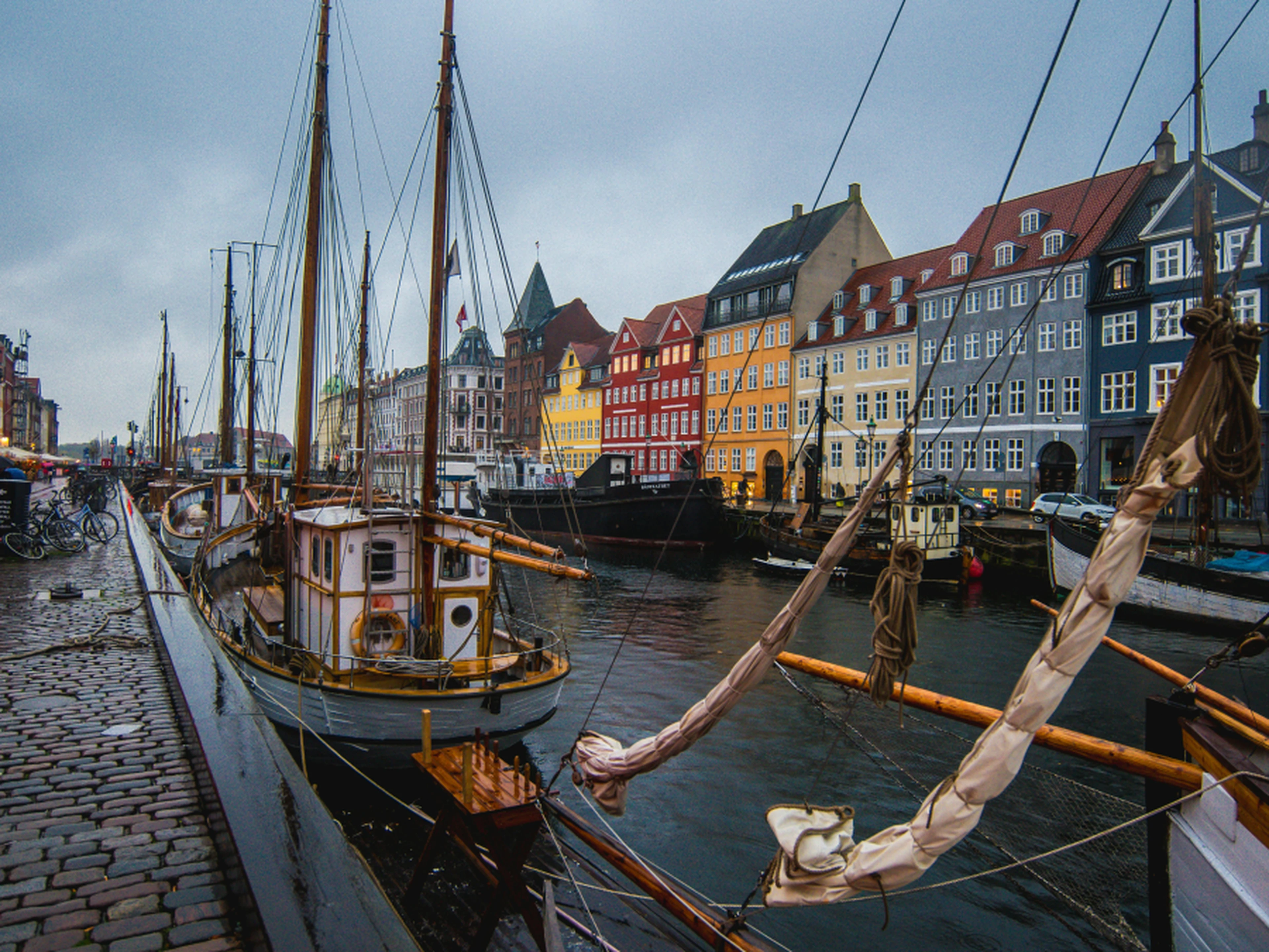 Colorful buildings line a canal with moored sailboats on a cloudy day, creating a picturesque waterfront scene.