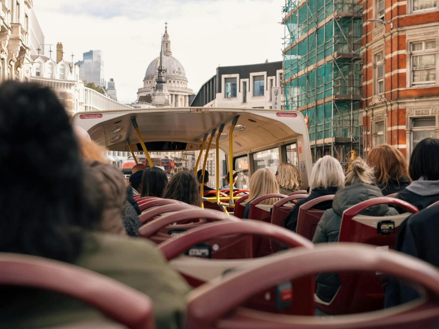 People on an open-top bus tour in a city with historic buildings and a view of a large dome in the background.