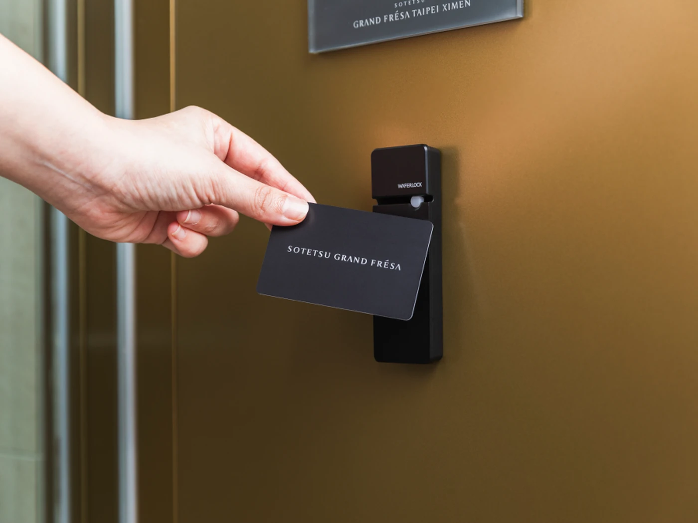 Hand holding a Sotetsu Grand Fresa key card to an electronic door lock on a gold hotel door.