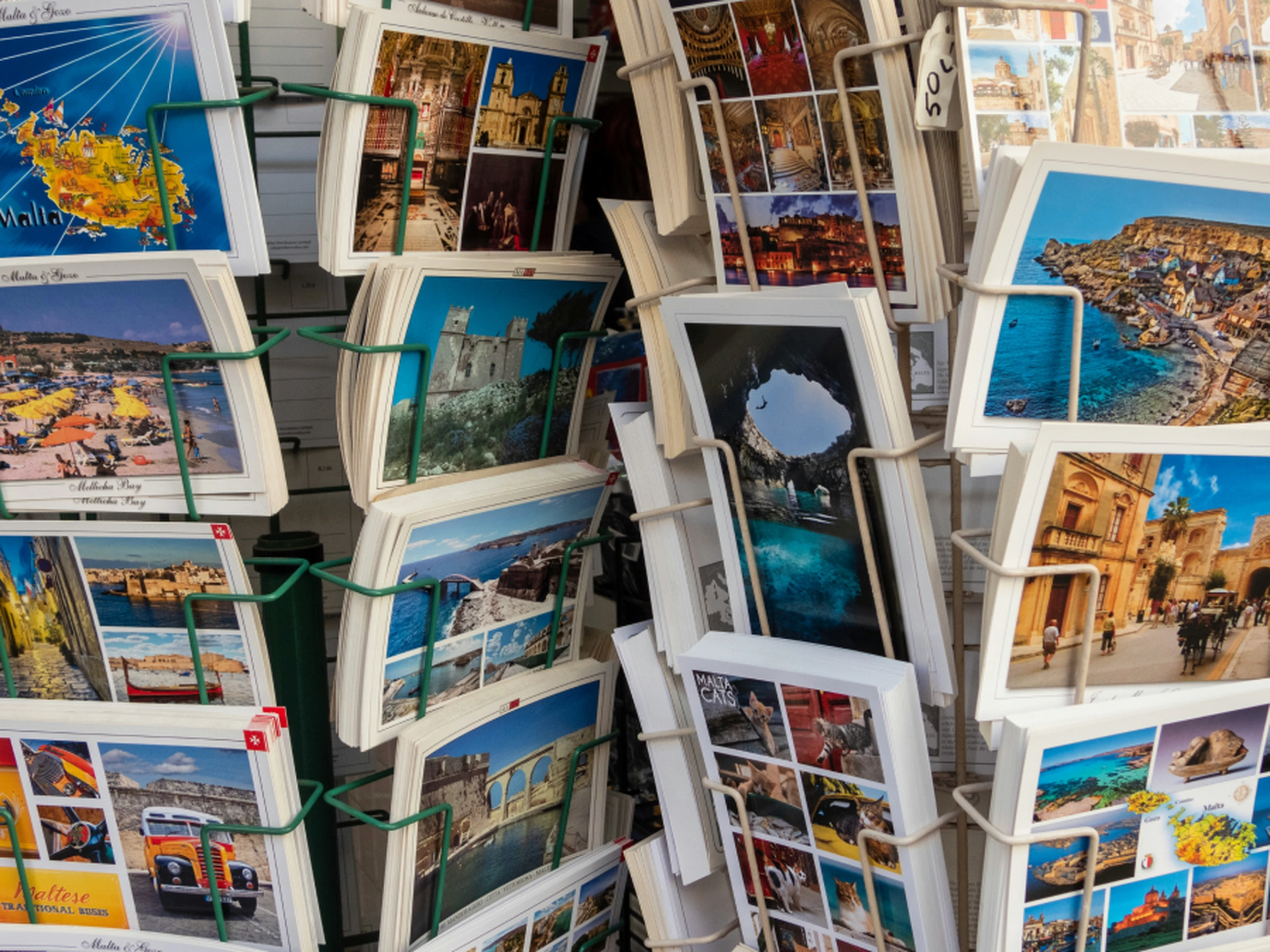 Rotating rack of colorful tourist postcards featuring beaches, seaside towns, historic buildings and scenic views.