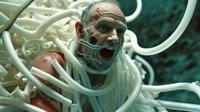 A man with a distressed expression entangled in numerous white tubes against a dark blue background.