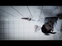 A man in a white shirt appears to be crawling on a tiled wall, looking upwards with a strained expression.