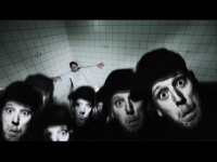 A person in white stands in a tiled room, surrounded by distorted, monochrome faces with wide eyes, creating a surreal, unsettling scene.