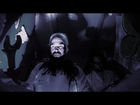 Two people in a dimly lit room, one in a lab coat like a doctor illuminated from below, creating dramatic shadows; the other partially obscured in darkness.