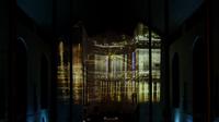 A dark church room with projected abstract light patterns resembling a cityscape reflected on water, projected onto the walls and ceiling over the altar.