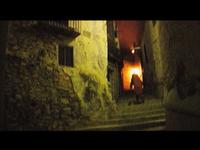 Dimly lit narrow alley with stone walls and steps, a person in a red cloak walking towards a warm light in the distance.