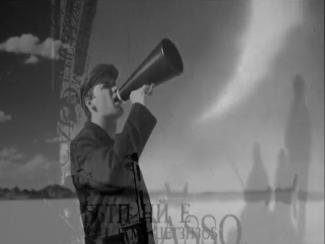 Black and white image of a young man speaking in a megaphone in front of a fluffy cloud sky.