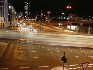 Nighttime city intersection with light trails from passing cars, illuminated streets, and tall buildings in the background.