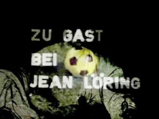 The image shows the text "Zu Gast bei Jean Löring" with a soccer ball graphic, projected onto a dark background.