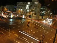 A nighttime city intersection with light trails from moving vehicles and illuminated buildings in the background.