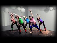 Five people in colorful workout attire perform synchronized dance moves in a studio with spherical lights and a patterned floor.