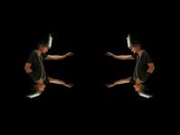 Two mirrored figures in dark attire and headpieces, reaching out against a black background, creating a symmetrical visual effect.