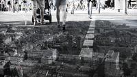 Aerial view of a cityscape blended with a street-level scene showing people walking on a sunny day.