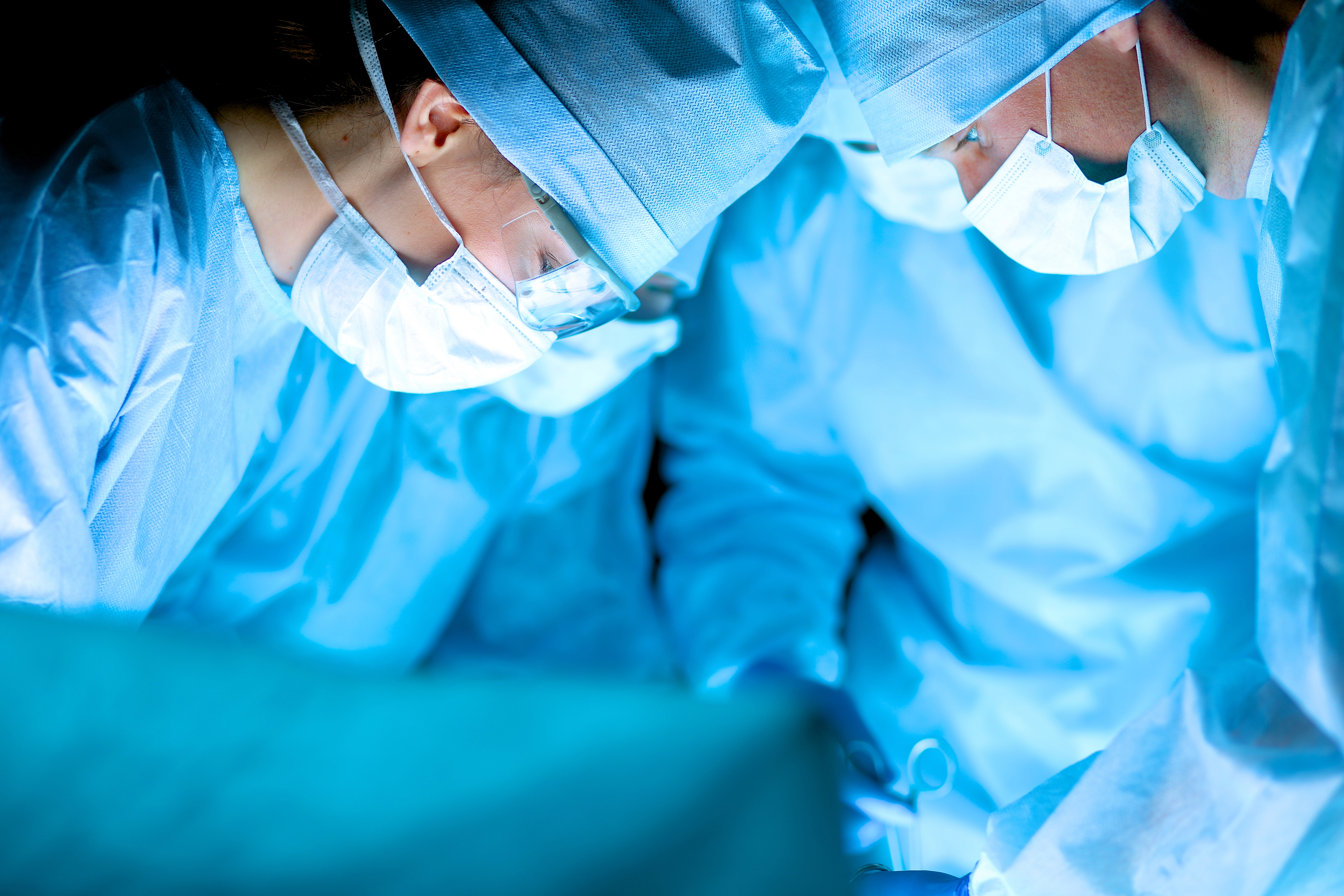 Surgeons in blue scrubs and masks focus intently on a medical procedure in an operating room.