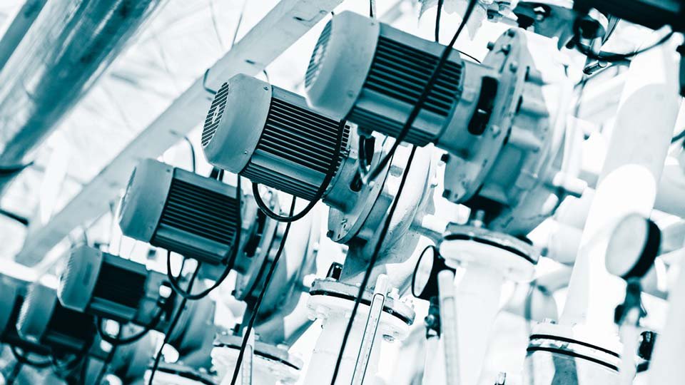Close-up of industrial electric motors lined up, attached to machinery with cables and pipes.