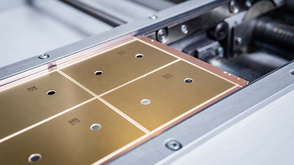 Close-up of a gold-colored metal plate with several small holes, set on a machine.