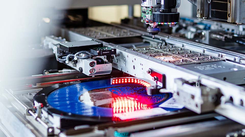 Close-up of a circuit board manufacturing machine with a blue wafer and red lighting, featuring robotic components and intricate machinery.