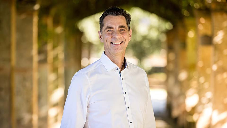 CEO Eckart Seitter smiling and standing in a sunny, vine-covered stone archway.