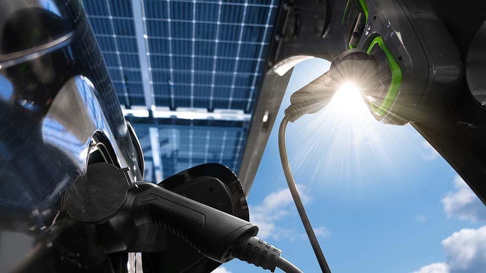 Electric vehicle charging under solar panels with sunlight shining through, highlighting sustainable energy usage.