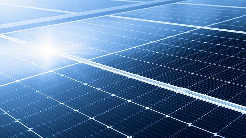 Close-up of solar panels under bright sunlight, highlighting their blue, reflective surfaces and grid-like patterns.