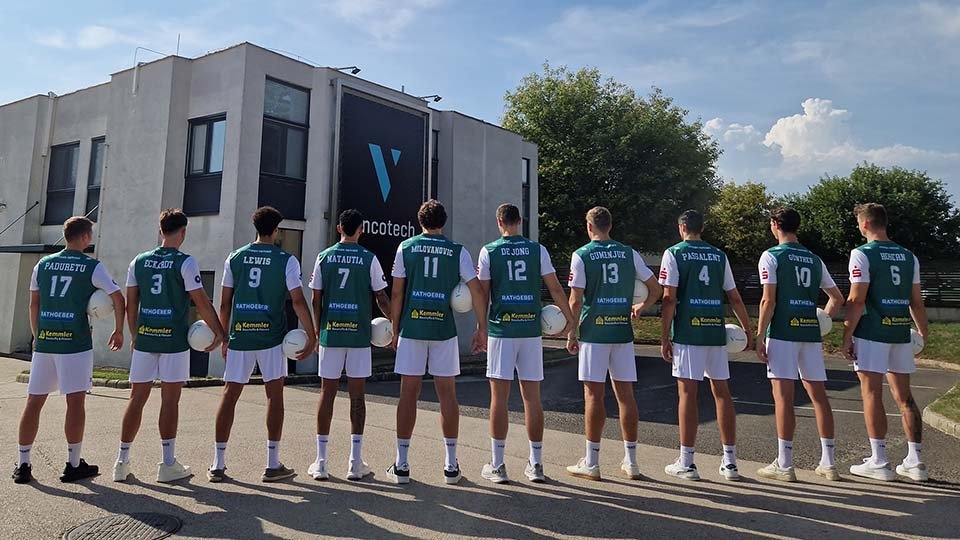 The volleyball team TSV Haching stands in a line, wearing matching green jerseys with numbers and white shorts, facing the Vincotech building.