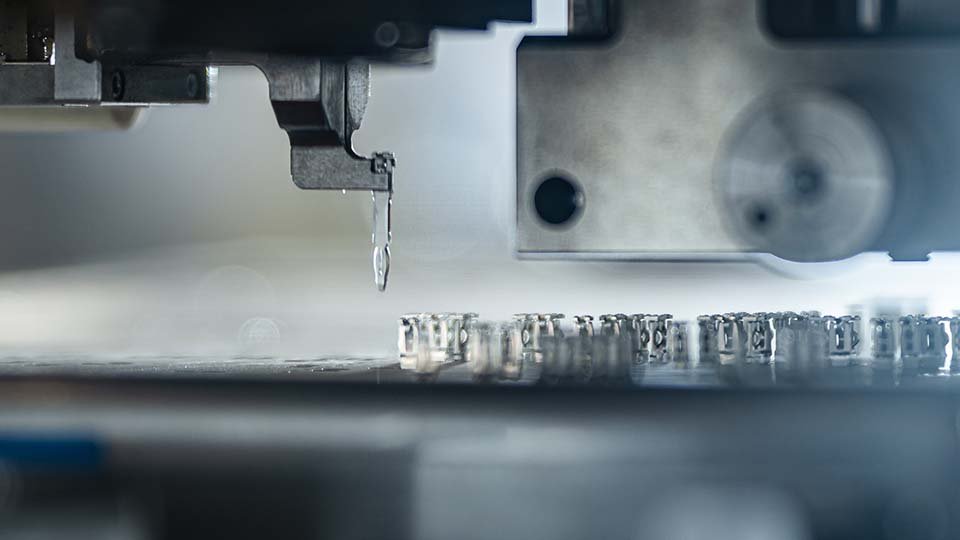 Close-up of a machine setting press-fit pins, with blurred background and intricate detailing.