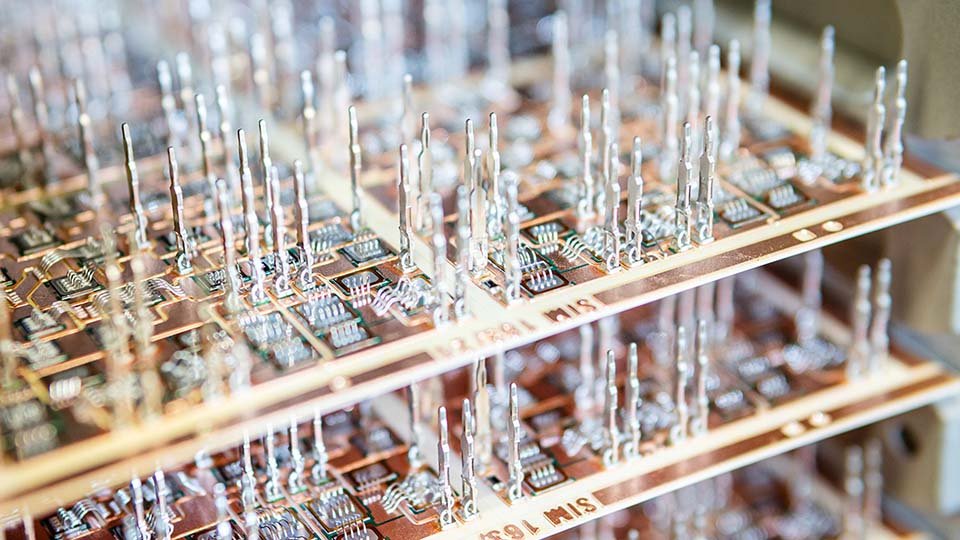 Close-up of layered circuit boards with numerous vertical press-fit pins, featuring intricate electronic components in a blurred perspective.