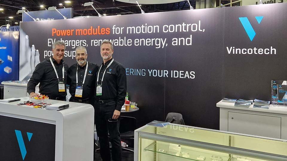 Three men in black shirts stand at a Vincotech booth showcasing power modules for motion control and renewable energy at APEC..