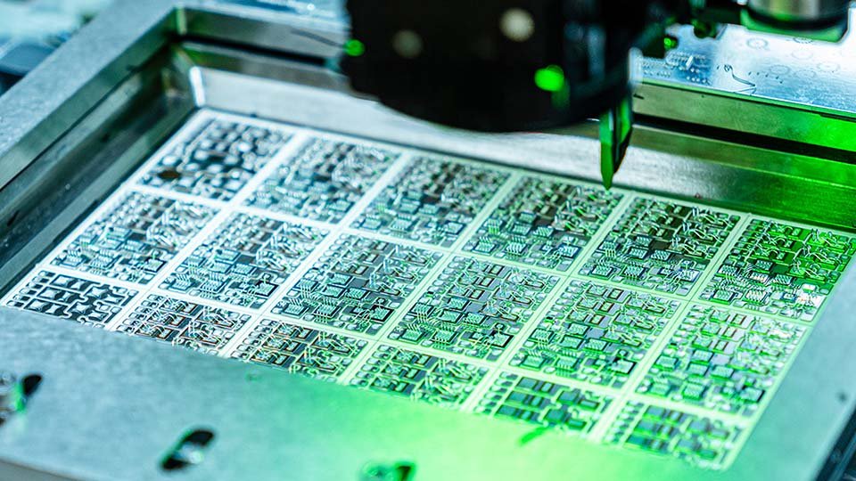 Close-up of a die-bonding machine, illuminated by green light in a manufacturing setting.