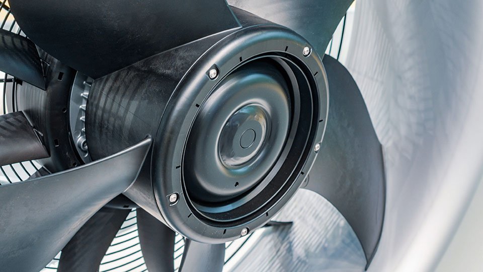 Close-up of a large black industrial fan with metallic blades and a circular hub, viewed from the side.