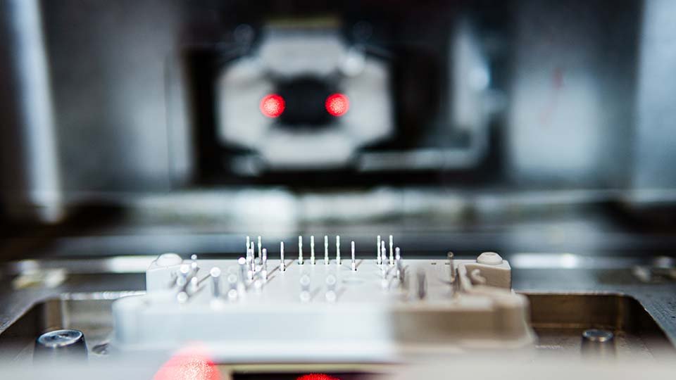 Close-up of a power module with metal pins in focus, and blurred red lights in the background.
