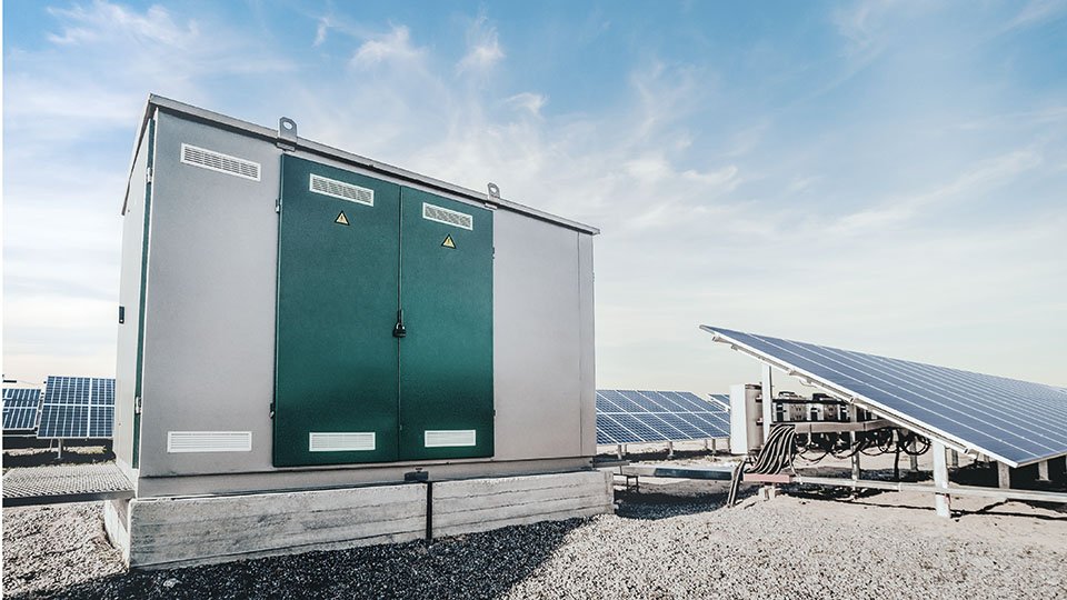 Solar power station with large electrical cabinet and solar panels under a clear sky.