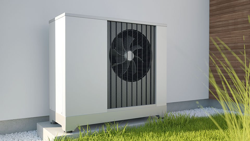Outdoor heat pump unit on a concrete slab next to a building, surrounded by green grass and white stones.