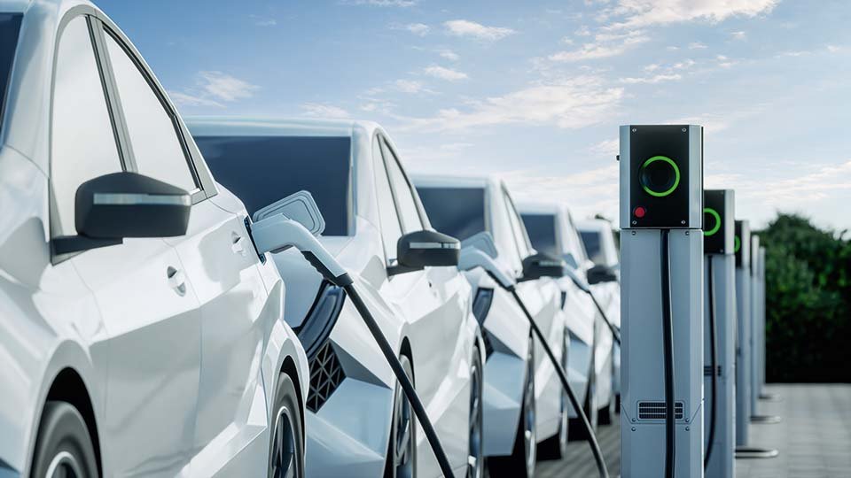 Row of white electric cars charging at charging stations under a blue sky.