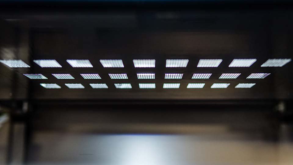 A grid of illuminated squares on a metallic surface, creating a pattern of light reflections in a dark setting.
