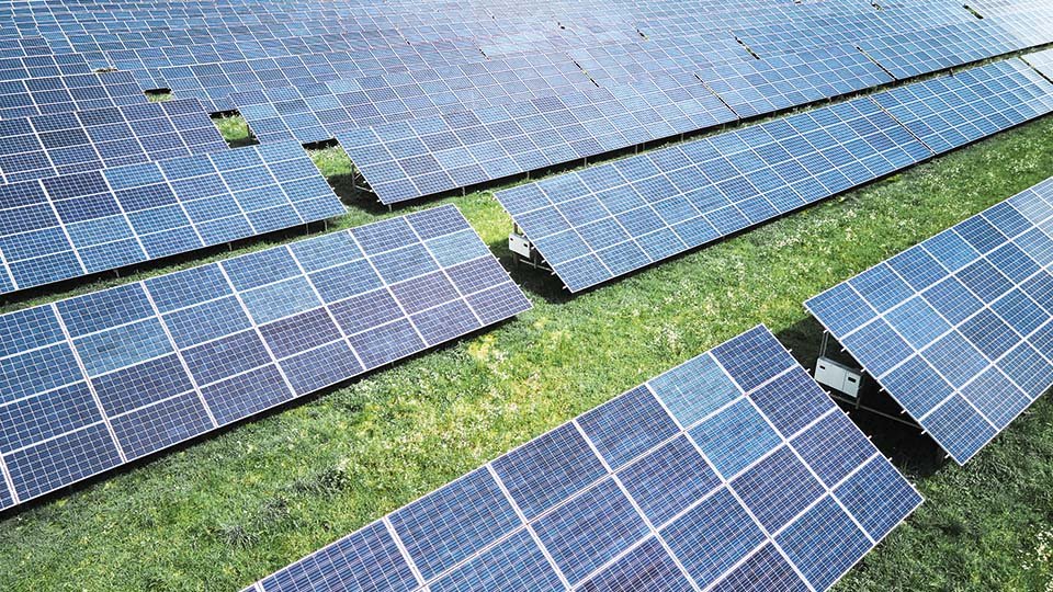 Aerial view of a solar farm with rows of solar panels installed on a grassy field, capturing sunlight for energy production.