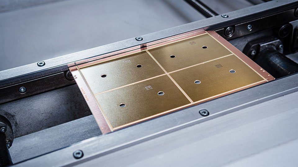 Close-up of a gold circuit board with four square sections, each with small holes, mounted in a machinery frame.