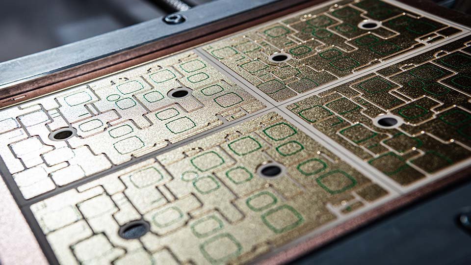 Close-up of a DCB substrate material with intricate gold patterns and multiple holes, showcasing its detailed electronic design.