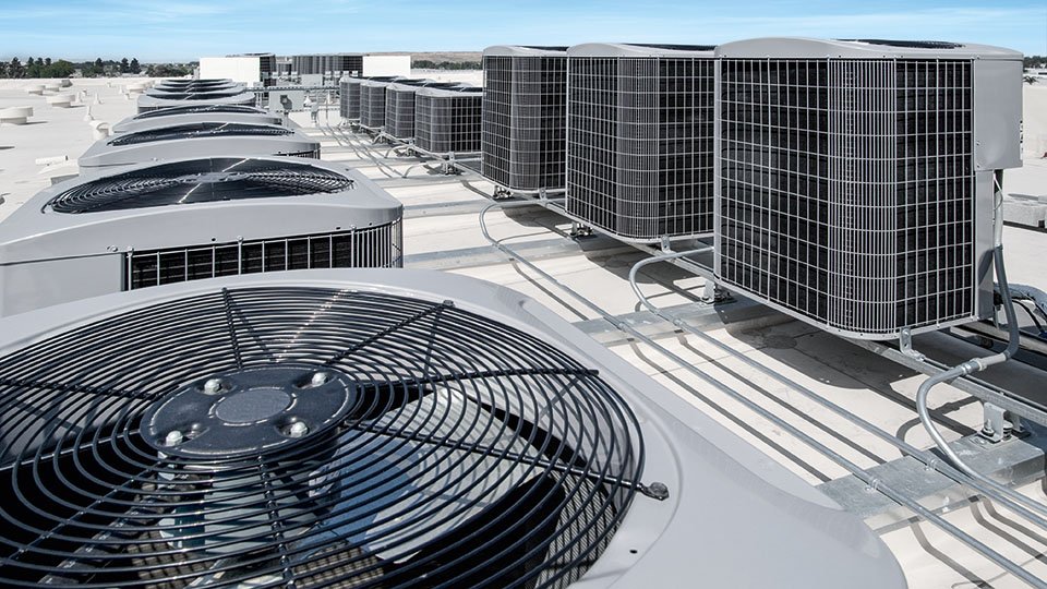 Rooftop view of multiple industrial air conditioning units with visible fan grilles and wiring under a clear blue sky.