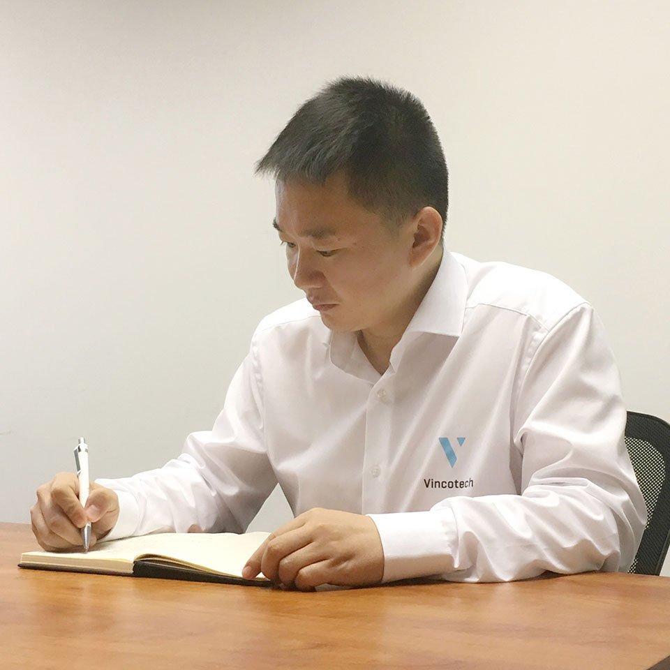 Eric writing in a notebook at a wooden table, in a minimalist office setting.