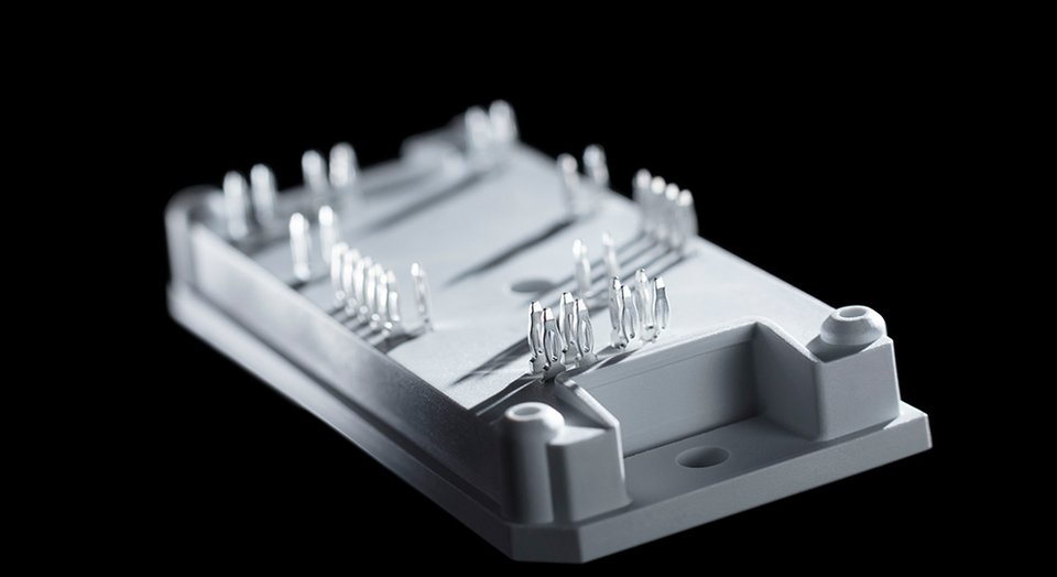 A close-up of a flow 0 module with multiple metal pins and a white plastic base against a black background.
